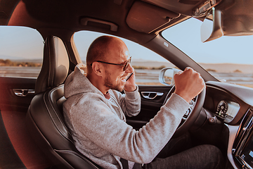 Image showing The driver receives happy information while talking on the smartphone while driving the car