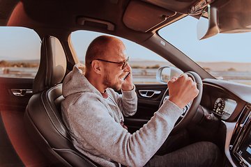 Image showing The driver receives happy information while talking on the smartphone while driving the car