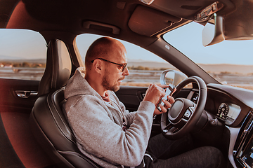 Image showing A man with a sunglasses driving a car and type a message on smartphone at sunset. The concept of car travel