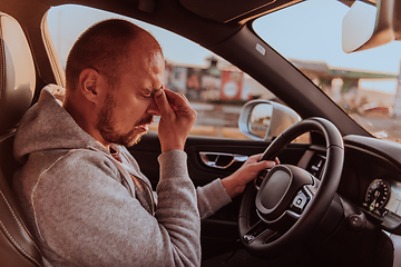 Image showing A tired driver holding his head. Exhausted and tired driver driving a car at sunset