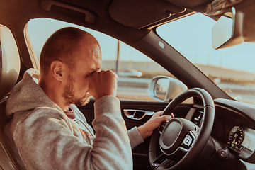 Image showing A tired driver holding his head. Exhausted and tired driver driving a car at sunset