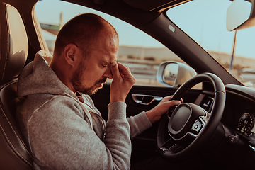 Image showing A tired driver holding his head. Exhausted and tired driver driving a car at sunset