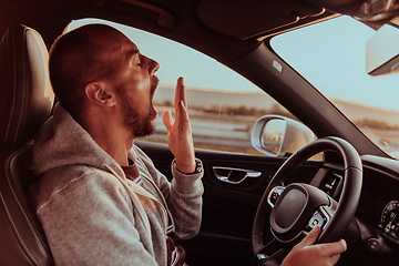 Image showing A tired driver yawns while driving a car at sunset