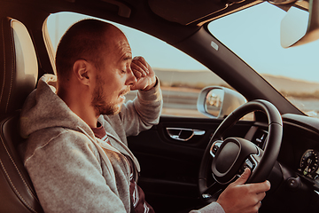 Image showing A tired driver holding his head. Exhausted and tired driver driving a car at sunset