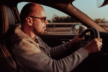 Image showing A man with a sunglasses driving a car at sunset. The concept of car travel