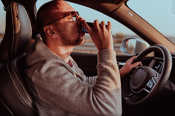 Image showing A tired man drinking acoffee while driving a car at sunset. Tired travel and long drive