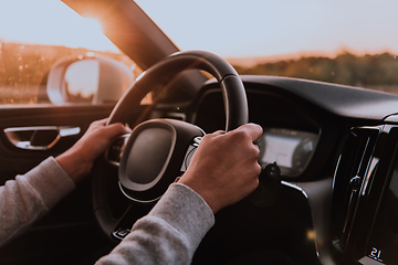 Image showing Close up man hand driving a car at sunset. The concept of car travel