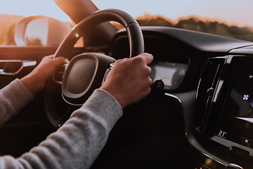 Image showing Close up man hand driving a car at sunset. The concept of car travel