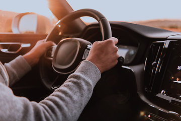 Image showing Close up man hand driving a car at sunset. The concept of car travel