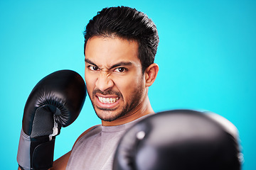 Image showing Angry boxer man, studio portrait and punch for workout, training and fitness by blue background. Athlete, boxing gloves and power for exercise, fight and development for performance in combat sports