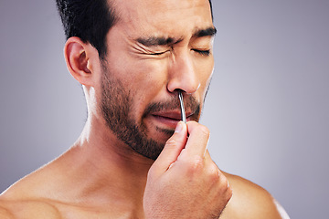 Image showing Plucking hair, nose and a man with tweezers for grooming, hygiene and beauty on a studio background. Pain, face and an Asian person with tools for cosmetics or facial care isolated on a backdrop