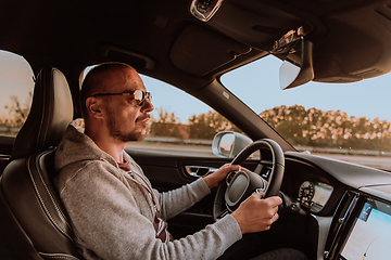 Image showing A man with a sunglasses driving a car at sunset. The concept of car travel