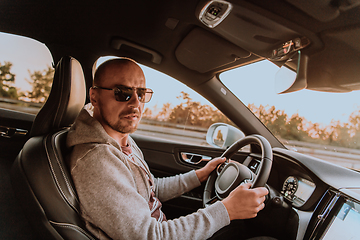 Image showing A man with a sunglasses driving a car at sunset. The concept of car travel