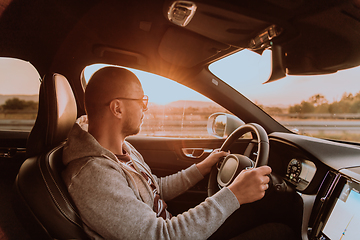 Image showing A man with a sunglasses driving a car at sunset. The concept of car travel