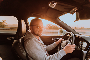 Image showing A man with a sunglasses driving a car at sunset. The concept of car travel