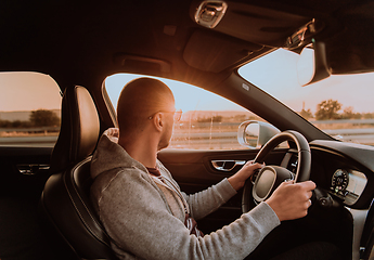 Image showing A man with a sunglasses driving a car at sunset. The concept of car travel