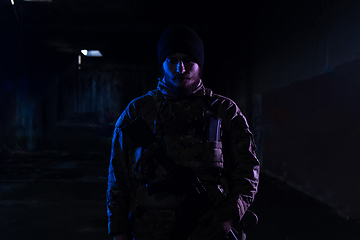 Image showing Army soldier in Combat Uniforms with an assault rifle and combat helmet night mission dark background. Blue and purple gel light effect.