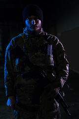 Image showing Army soldier in Combat Uniforms with an assault rifle and combat helmet night mission dark background. Blue and purple gel light effect.