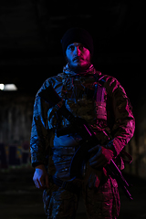 Image showing Army soldier in Combat Uniforms with an assault rifle and combat helmet night mission dark background. Blue and purple gel light effect.