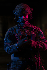 Image showing Photo of a fully equipped soldier in black armor tactical vest and gloves standing on black background closeup front view.