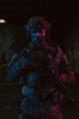 Image showing Army soldier in Combat Uniforms with an assault rifle and combat helmet night mission dark background. Blue and purple gel light effect.