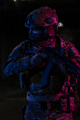 Image showing Army soldier in Combat Uniforms with an assault rifle and combat helmet night mission dark background. Blue and purple gel light effect.