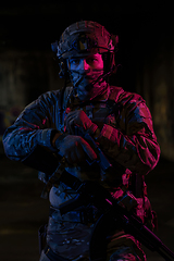 Image showing Army soldier in Combat Uniforms with an assault rifle and combat helmet night mission dark background. Blue and purple gel light effect.