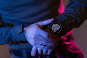 Image showing Modern warfare soldier checking navigation, time and other information on a smartwatch. Dark night black background.