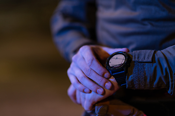 Image showing Modern warfare soldier checking navigation, time and other information on a smartwatch. Dark night black background.