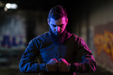 Image showing Photo of a fully equipped soldier in black armor tactical vest and gloves standing on black background closeup front view.