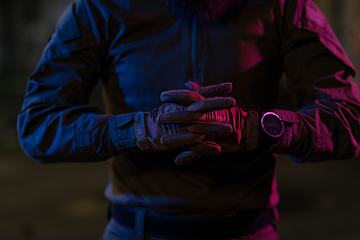 Image showing Photo of a fully equipped soldier in black armor tactical vest and gloves standing on black background closeup front view.