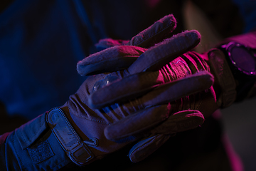 Image showing Photo of a fully equipped soldier in black armor tactical vest and gloves standing on black background closeup front view.