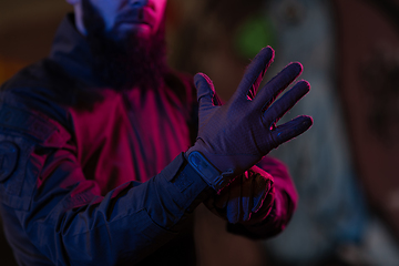 Image showing Photo of a fully equipped soldier in black armor tactical vest and gloves standing on black background closeup front view.