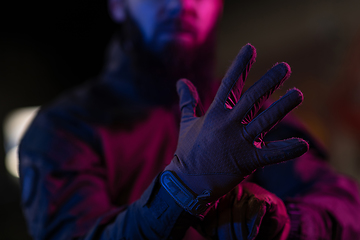 Image showing Photo of a fully equipped soldier in black armor tactical vest and gloves standing on black background closeup front view.