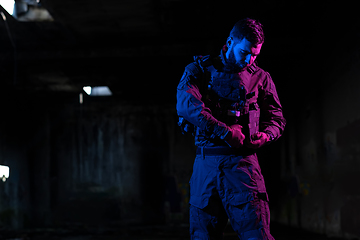 Image showing Army soldier in Combat Uniforms with an assault rifle and combat helmet night mission dark background. Blue and purple gel light effect.