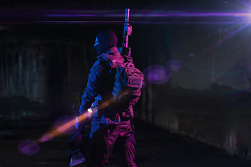 Image showing Army soldier in Combat Uniforms with an assault rifle and combat helmet night mission dark background. Blue and purple gel light effect.