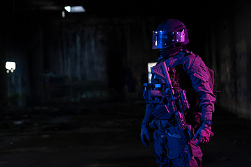 Image showing Army soldier in Combat Uniforms with an assault rifle and combat helmet night mission dark background. Blue and purple gel light effect.