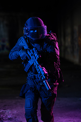 Image showing Army soldier in Combat Uniforms with an assault rifle and combat helmet night mission dark background. Blue and purple gel light effect.