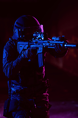 Image showing Army soldier in Combat Uniforms with an assault rifle and combat helmet night mission dark background. Blue and purple gel light effect.