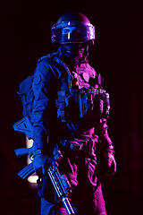 Image showing Army soldier in Combat Uniforms with an assault rifle and combat helmet night mission dark background. Blue and purple gel light effect.