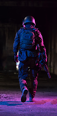 Image showing Army soldier in Combat Uniforms with an assault rifle and combat helmet night mission dark background. Blue and purple gel light effect.