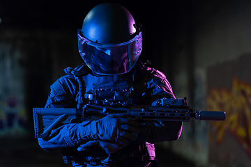 Image showing Army soldier in Combat Uniforms with an assault rifle and combat helmet night mission dark background. Blue and purple gel light effect.