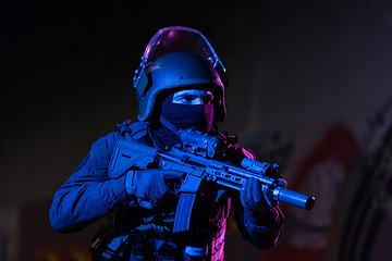 Image showing Army soldier in Combat Uniforms with an assault rifle and combat helmet night mission dark background. Blue and purple gel light effect.