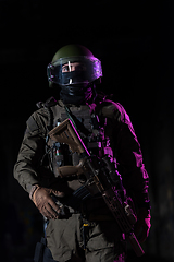 Image showing Army soldier in Combat Uniforms with an assault rifle and combat helmet night mission dark background. Blue and purple gel light effect.