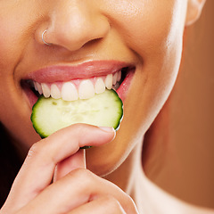 Image showing Woman, mouth or eating a cucumber for skincare nutrition or healthy diet against a brown studio background. Smile, bite or closeup of girl vegetable for organic facial treatment or natural cosmetics