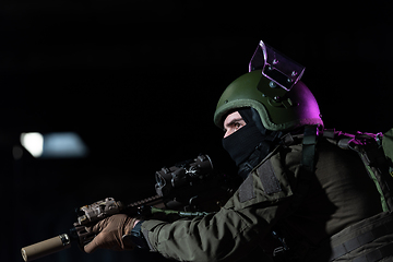 Image showing Army soldier in Combat Uniforms with an assault rifle and combat helmet night mission dark background. Blue and purple gel light effect.