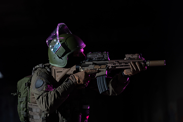 Image showing Army soldier in Combat Uniforms with an assault rifle and combat helmet night mission dark background. Blue and purple gel light effect.