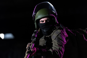 Image showing Army soldier in Combat Uniforms with an assault rifle and combat helmet night mission dark background. Blue and purple gel light effect.