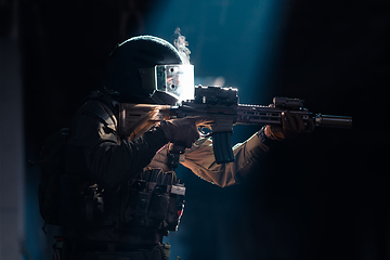 Image showing Army soldier in Combat Uniforms with an assault rifle and combat helmet night mission dark background. Blue and purple gel light effect.