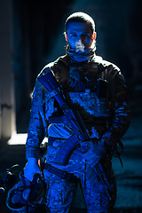 Image showing Army soldier in Combat Uniforms with an assault rifle and combat helmet night mission dark background. Blue and purple gel light effect.